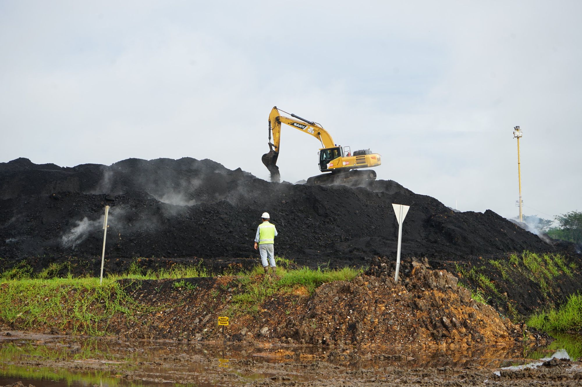 Excavator bekerja di atas stockpile batubara, diawasi petugas lapangan